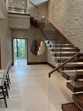 Walnut cantilever stair with frameless glass and wood handrail beside a round mirror