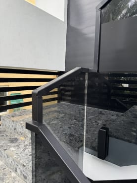 Solar gray tinted glass on side-mounted talons with a black handrail on terrazzo stairs