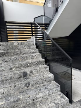 Terrazzo stairs with solar gray glass panels on side-mount talons and a black handrail