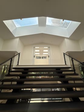 Wide dark-tread floating stair with post glass railings leading up toward skylights
