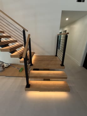 White oak floating treads with LED lighting and onyx black rod railing at the base of a mono stair