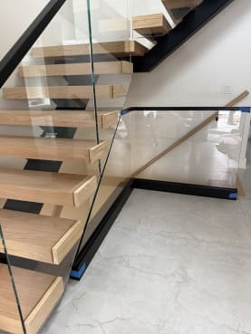 White oak floating treads on a black mono stringer with frameless glass and a black base rail on marble floors