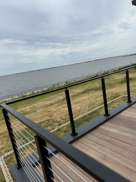 Black surface-mount rod railing on an ipe deck overlooking a wide bay
