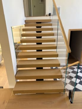 Straight white oak FLIGHT Mono stair with frameless glass on black talons and a wood handrail above a checkered floor
