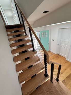 Red oak floating stair on a black mono stringer with black cable railing and oak handrail in a bright beach-house entry
