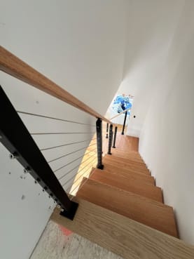 Looking down red oak floating treads with black cable railing and oak handrail