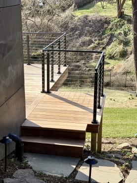 Black cable railing wraps an ipe deck and steps above a stone path