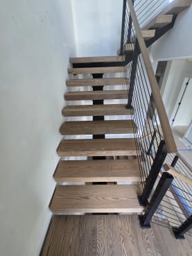 Red oak floating treads on a black mono stringer with black rod railing and oak handrail turning at a landing