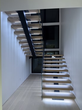 Pale oak floating switchback stair with cool LED tread lighting and frameless glass