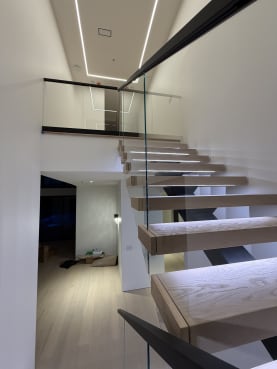 Oak floating treads with LED strips beside frameless glass and a linear light ceiling