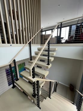 Whitewashed oak switchback floating stair with black cable railing and slat screen loft above