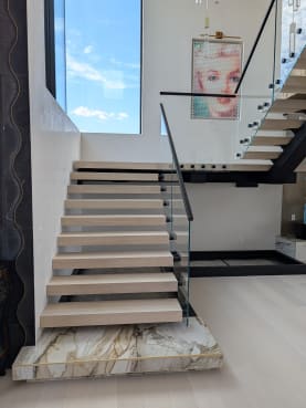 White oak floating treads rising from a gold-veined marble plinth with frameless glass and black handrail
