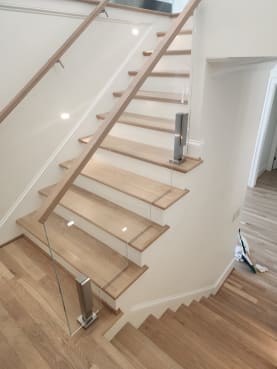 Frameless glass on brushed stainless posts with an oak cap rising beside a white oak stair