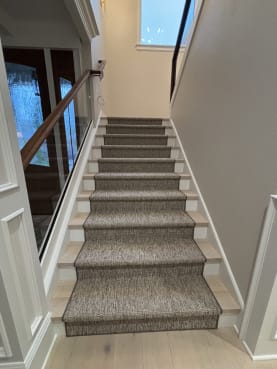 Frameless base rail glass with a dark walnut cap along a stair with a woven runner and white trim