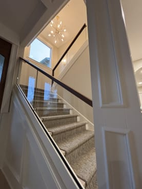 Frameless base rail glass with a dark walnut cap along a stair with a woven runner and white trim