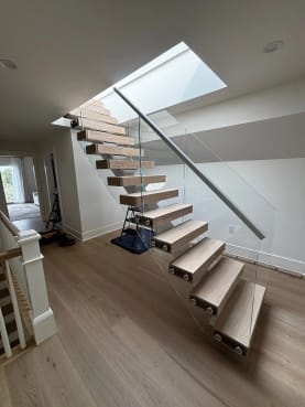 Thick white oak floating treads on a white mono stringer with frameless glass rising to a skylight