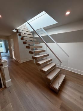 White oak floating stair with frameless glass and slim handrail climbing toward a bright skylight