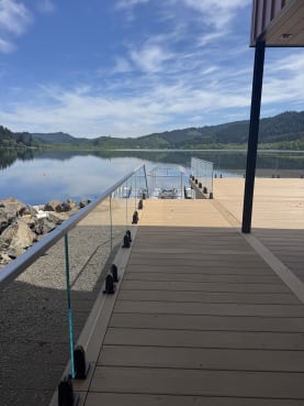 Frameless glass on dark talon spigots lines a composite deck reaching out over a calm mountain lake