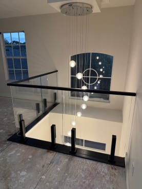 Frameless glass on black talons with a black cap overlooks a two-story foyer with a glowing orb pendant