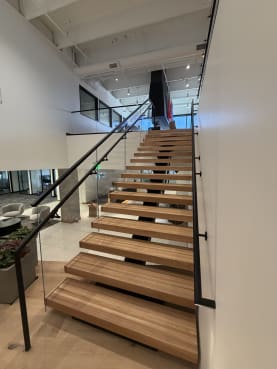 Straight run of wood floating treads with glass railing and black wall handrail in an office