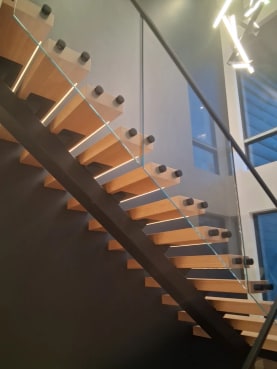 White oak floating treads with LED strips on a black mono stringer beside frameless glass and a black handrail