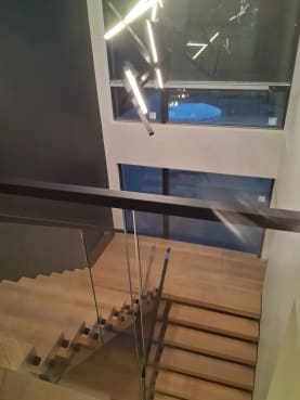 White oak floating switchback treads beside frameless standoff-pin glass and a black handrail