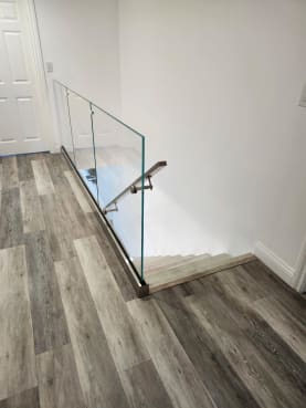 Frameless glass in a stainless base rail with a stainless wall handrail at the top of a stair