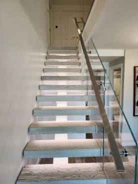Straight run of gray-oak floating treads with LED lighting, frameless glass and a square stainless handrail