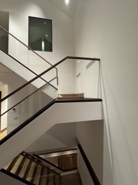 Frameless base rail glass with walnut handrails rising through a three-story stairwell