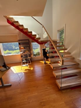Ash floating treads on a bold red mono stringer with frameless glass and an ash top cap in a sunlit room