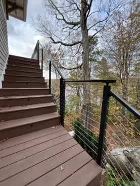 Black cable railing follows composite stairs down through autumn trees by a lake