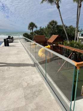 Frameless glass in a base rail edges a stone terrace with palms and the Gulf beyond