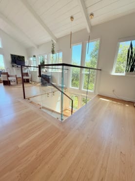 A glass railing with a walnut handrail surrounds a stair opening in a sunlit vaulted living space.