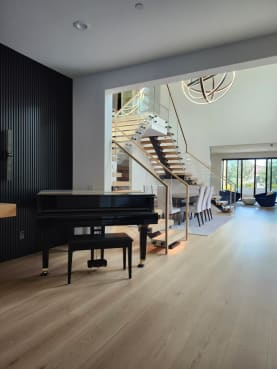 A grand piano sits in the foreground with FLIGHT Mono stairs and standoff-pin glass railing in the room beyond.