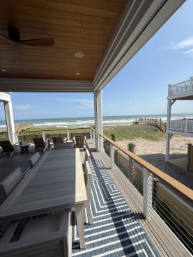 Cable railing with white posts and a wood top rail on a covered porch with dining table facing the ocean.