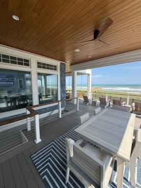 Cable railing with wood cap rail along a covered beach-house porch with outdoor dining.
