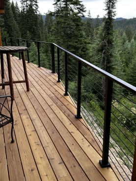 Black cable railing on a cedar deck overlooking a forested mountain valley.