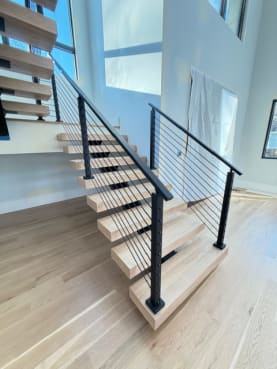 Close view of white oak floating treads on a black mono stringer with black cable railing at the stair base.