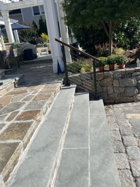Black cable railing with a wood handrail runs beside bluestone steps leading to a stone patio.