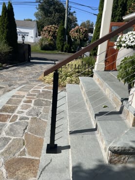 A black-post cable railing with wood handrail follows bluestone entry steps to a front porch.