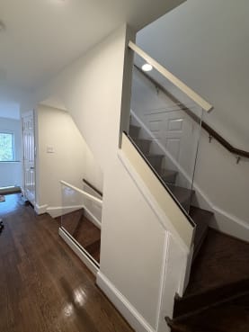 Frameless glass panel with white cap guards a dark-stained stair alongside a wall-mounted wood handrail.