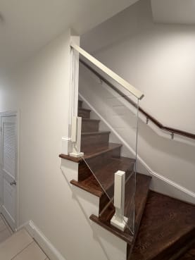 Frameless glass railing with a white cap rail beside a dark wood winder stair and wall handrail.