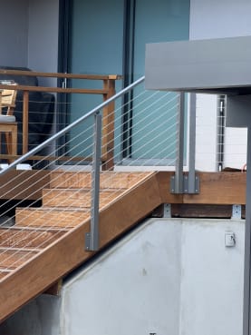 Gray-post cable railing follows a hardwood exterior stair above a concrete wall.