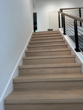 Light oak stair treads climb beside a black rod railing with wood handrail.