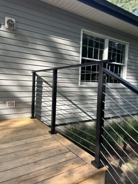 Black-post cable railing surrounds a cedar landing at a gray-sided home.