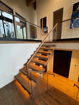 Oak floating treads with LED under-lighting turn at a landing beneath a glass balcony guard with wood handrail.