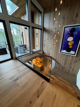 A frameless glass guard set in a black base channel wraps the stair opening beneath tall windows and a pendant chandelier.