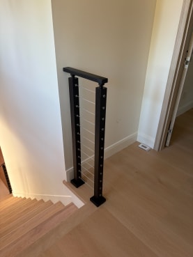 A black cable railing section with a flat black top rail guards the top of a light oak stair.