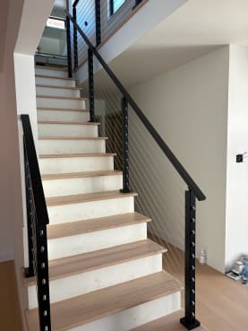 Black posts and handrails with stainless cables flank a straight white-riser oak stair.