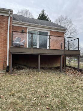A raised composite deck on a red brick home is enclosed by dark posts with glass panels.